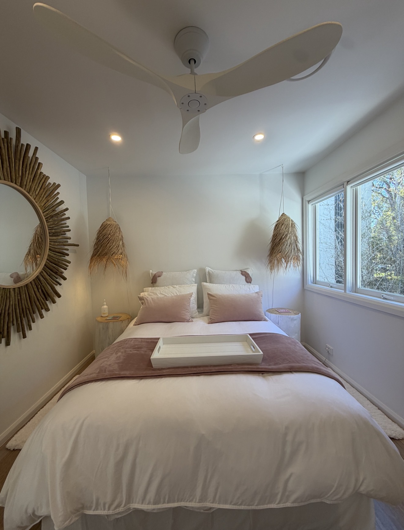 Bedroom with driftwood sunburst mirror, mauve throw, white breakfast tray and grass pendant lights
