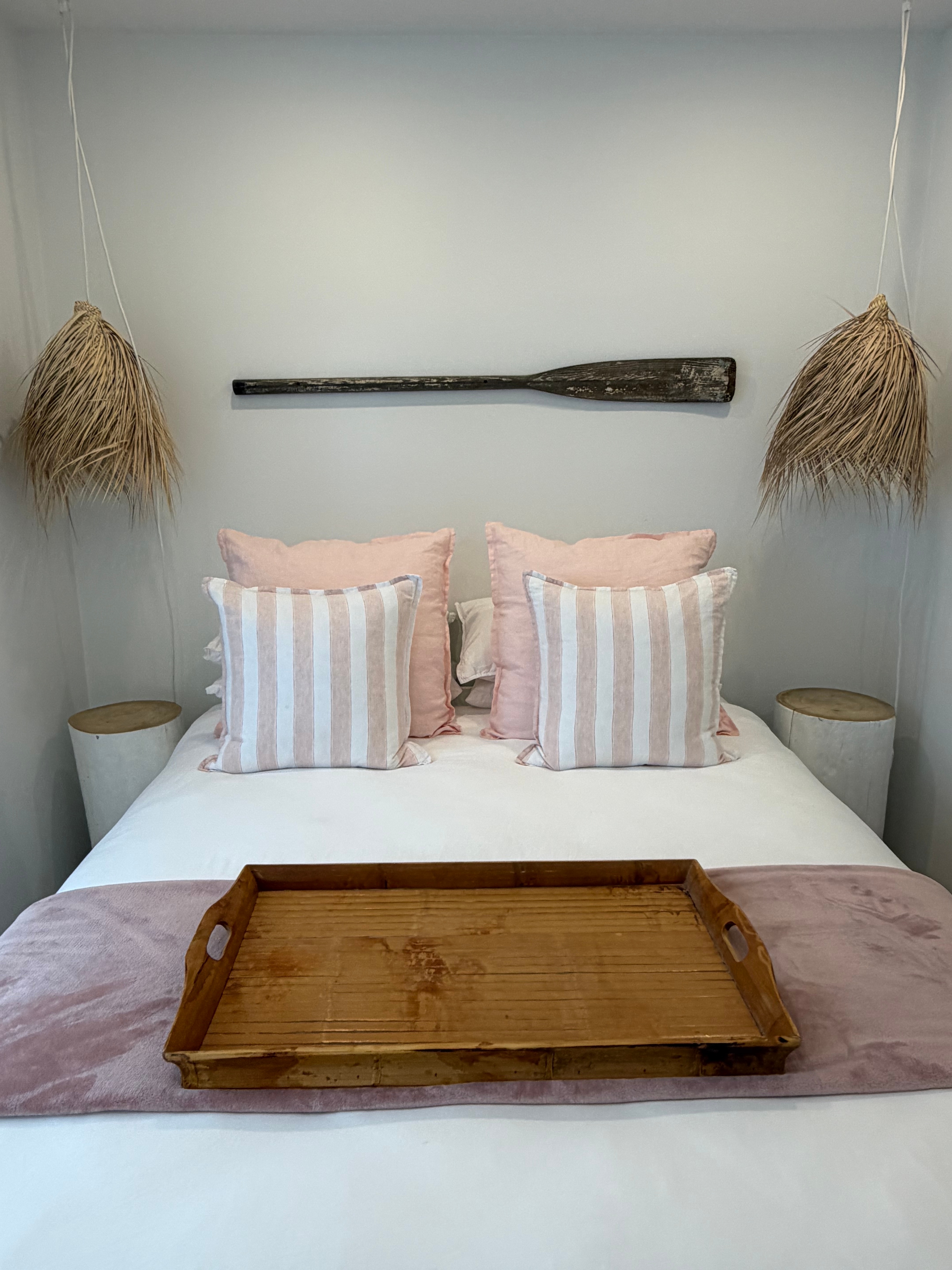 Bedroom with pink striped pillows, rattan pendants and wooden oar wall art
