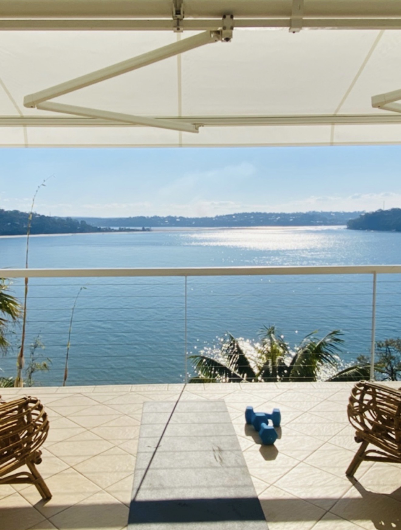 Yoga mat and dumbbells on a balcony overlooking the bay under a white awning