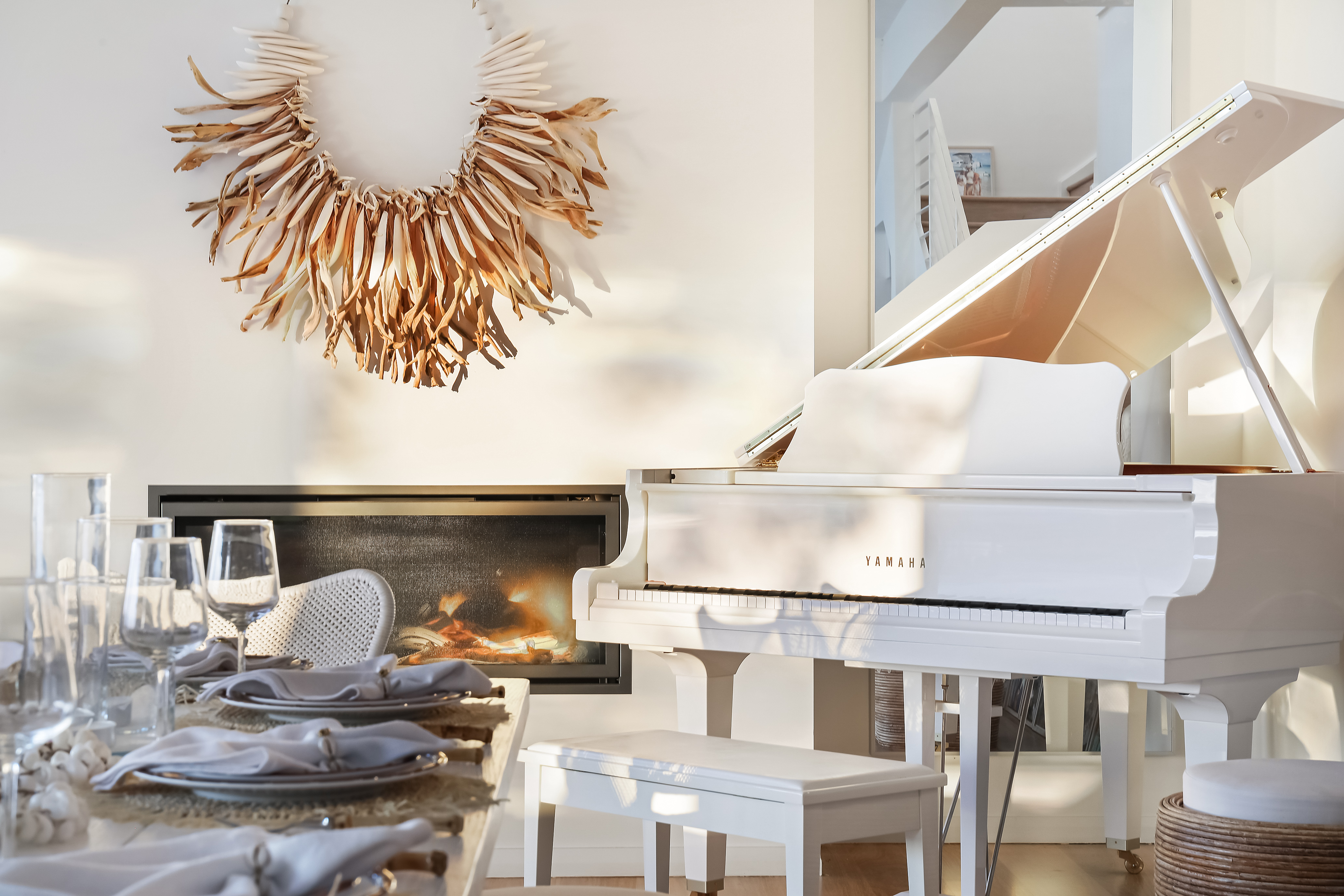 White Yamaha grand piano beside a lit fireplace with dressed dining table