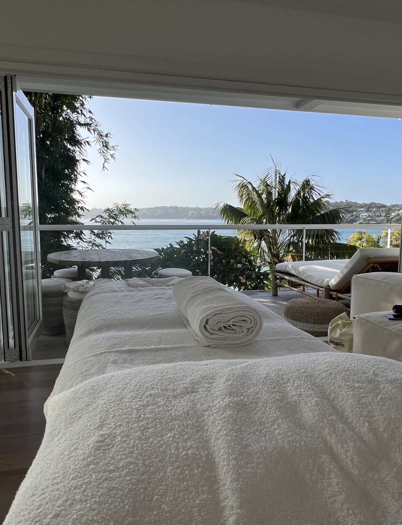 Spa massage bed with rolled towel on a balcony overlooking the bay and loungers
